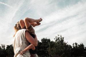 A couple in white wedding attire embraces and kisses during their outdoor photoshoot with cloudy skies in the background.
