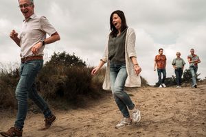 People walking along a sandy beach trail on an overcast day with coastal vegetation in the background.