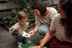 A person in a striped shirt uses a green plastic bottle to create a DIY project outdoors.