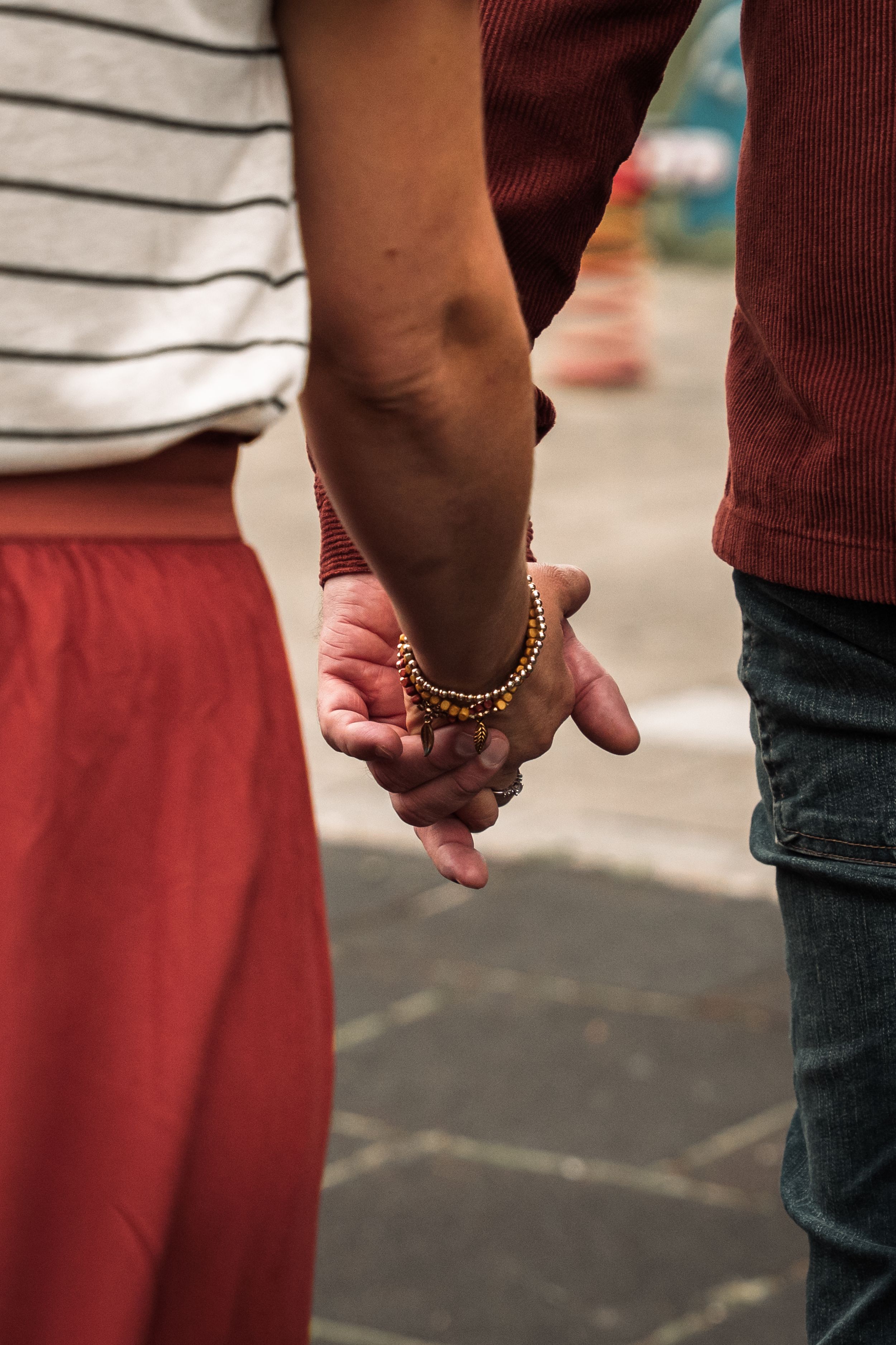 Close-up of two people holding hands with one wearing a striped shirt and red pants, and the other in burgundy pants.