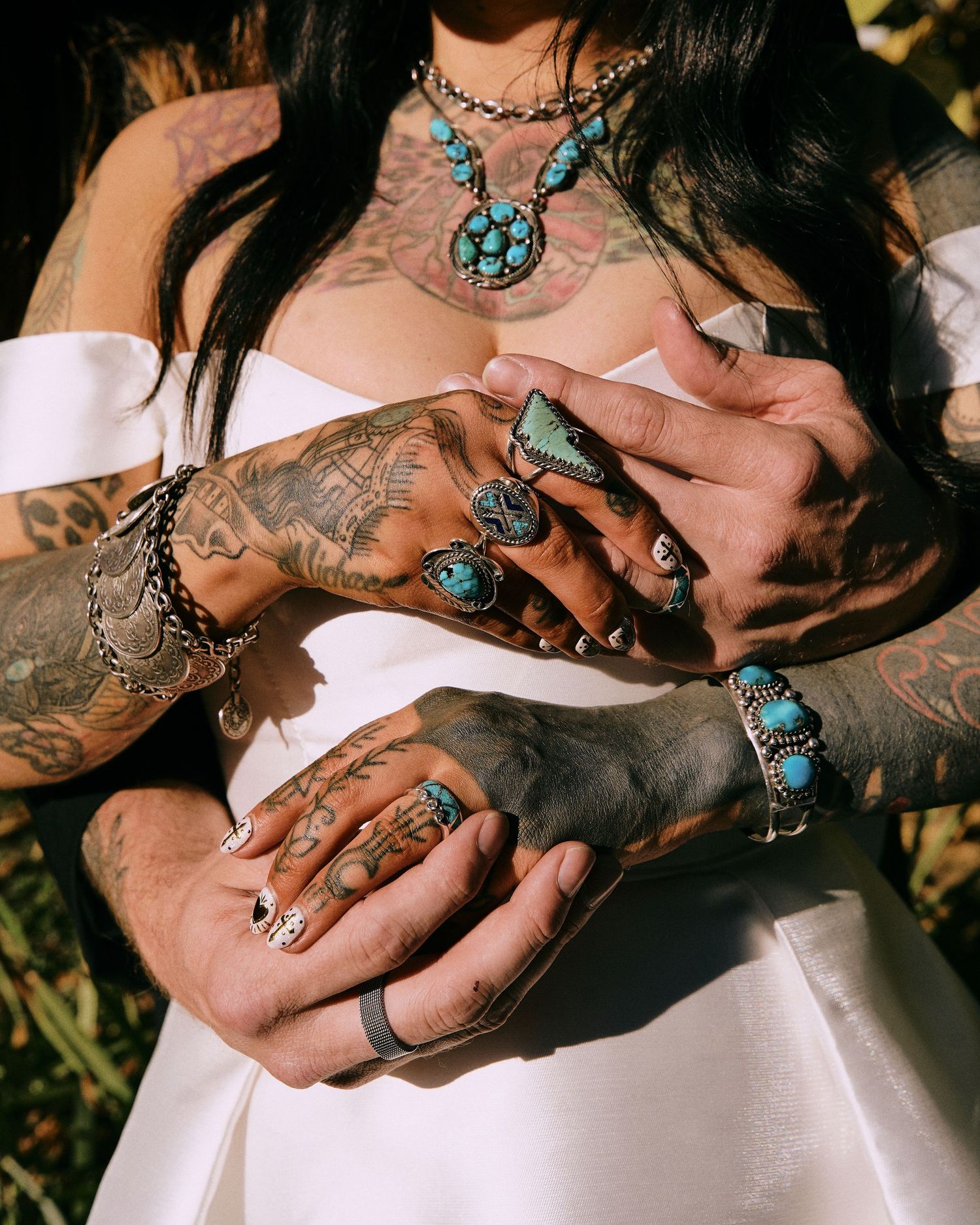 Close-up of hands wearing turquoise jewelry and rings in sunlight. Editorial wedding photo featuring detail shot of rings on tattooed arms.