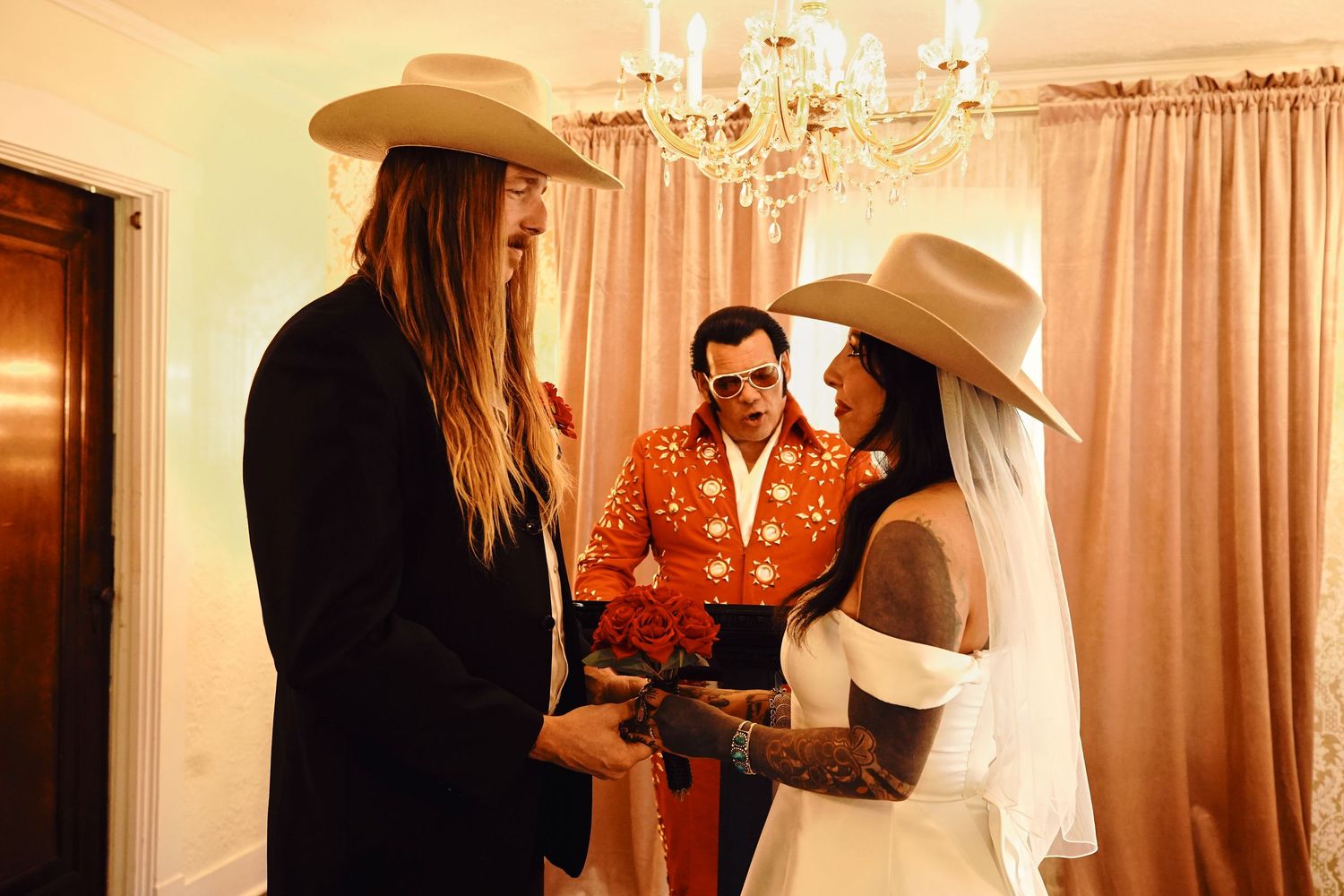 A group in western and formal attire gather in a room with elegant decor and warm lighting.
