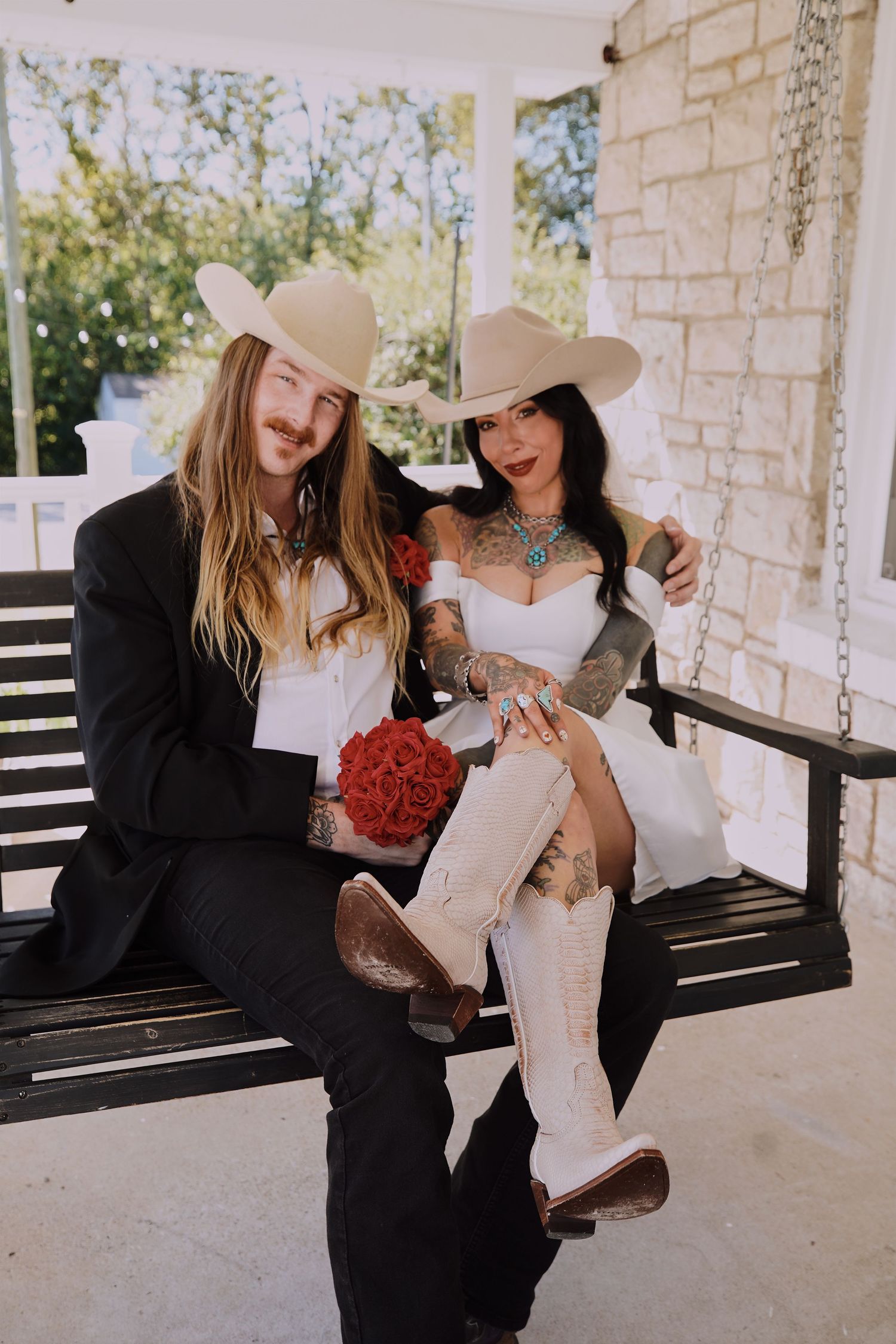 married couple sharing laughs while sitting on a porch swing at a rustic stone building.