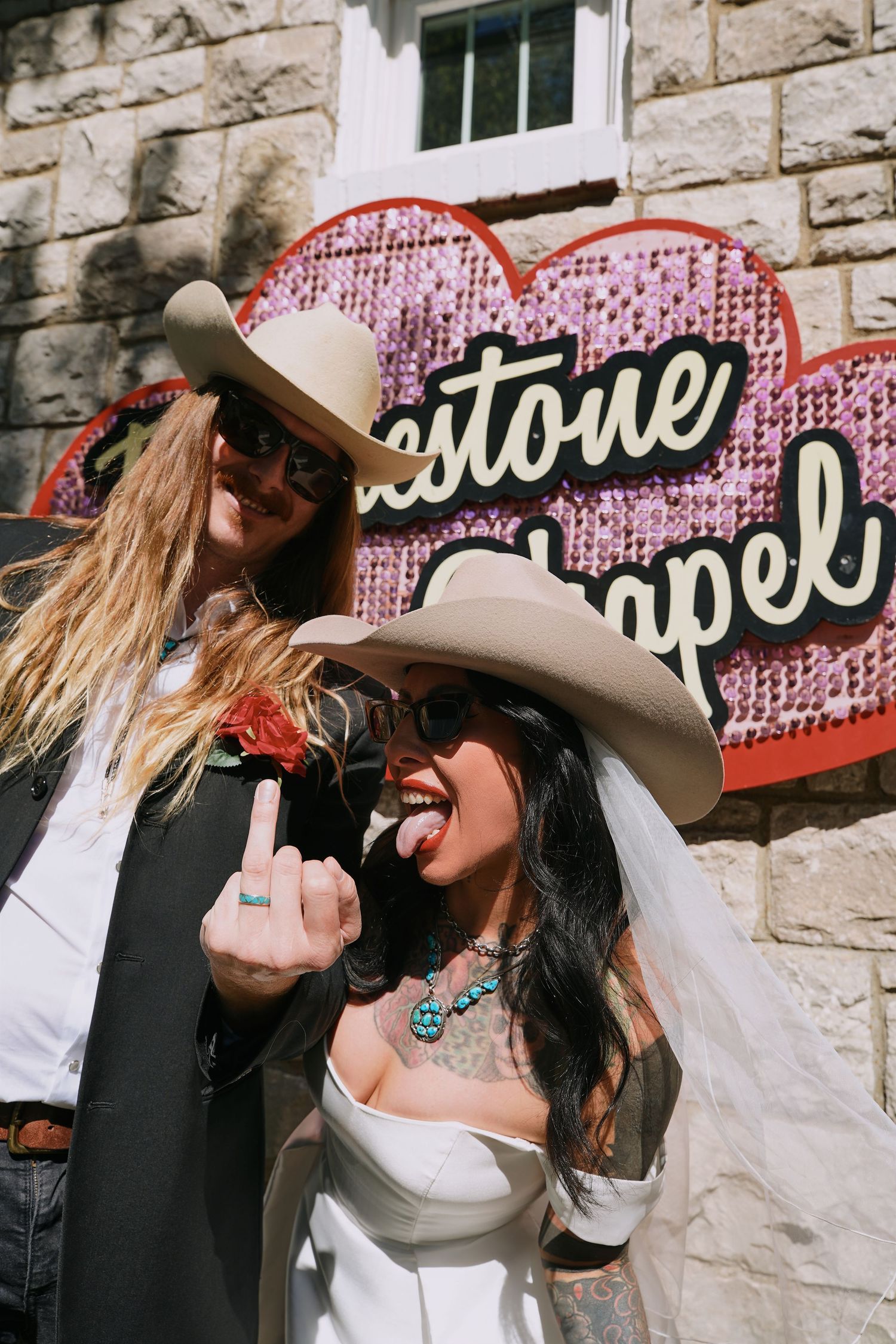 newly married couple together against a stone wall with vintage neon signage.