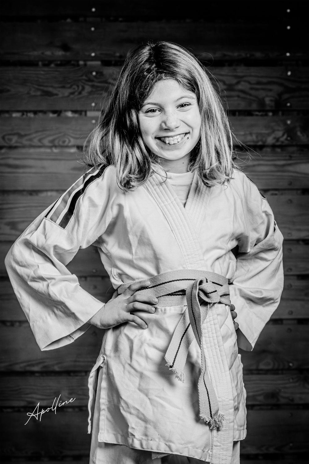 Smiling young girl in white judo gi with orange belt poses in black and white portrait.