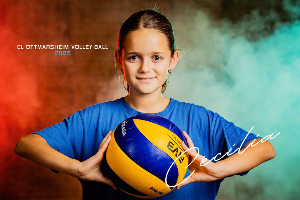 Young girl Cecilia in blue jersey holds yellow and blue volleyball in colorful smoke portrait.