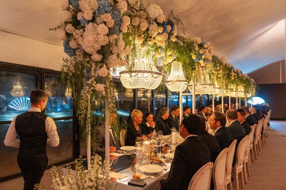 Elegant dinner party setting with crystal chandelier and floral arch decorations over a long dining table.