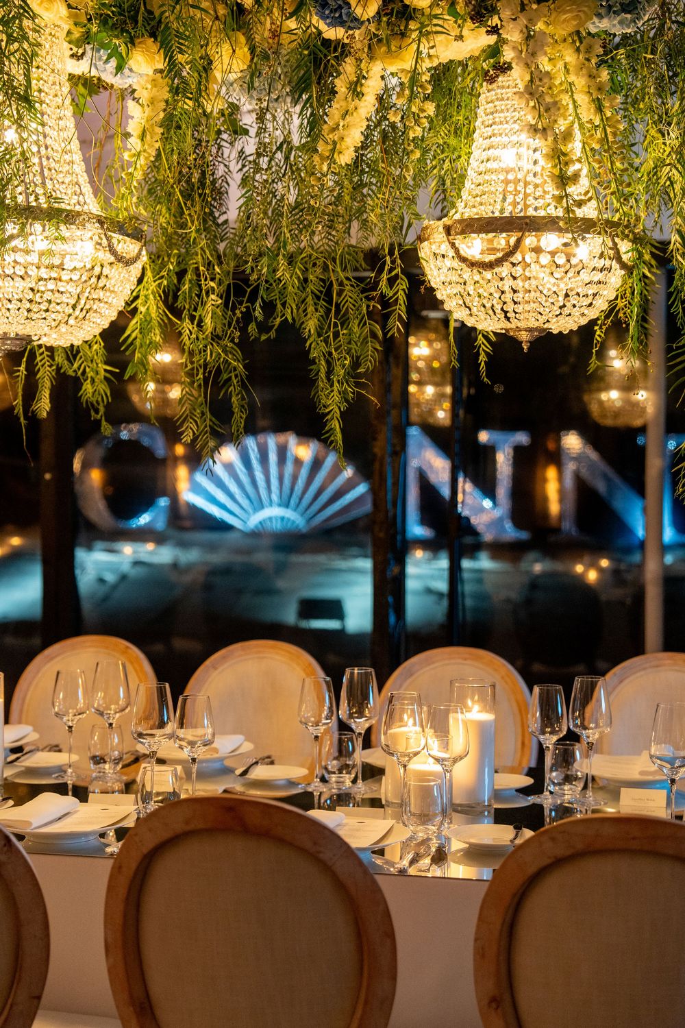 Elegant wedding reception table setting with crystal chandeliers and hanging greenery creating a romantic atmosphere.