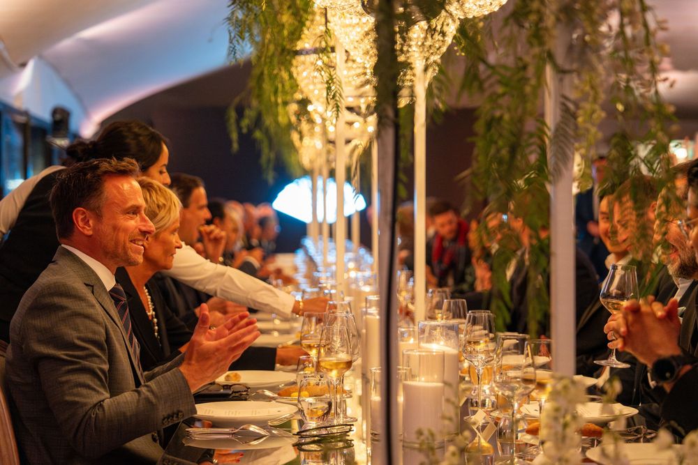 Guests enjoying an elegant candlelit dinner party at a long table decorated with floral centerpieces and glowing ambiance.