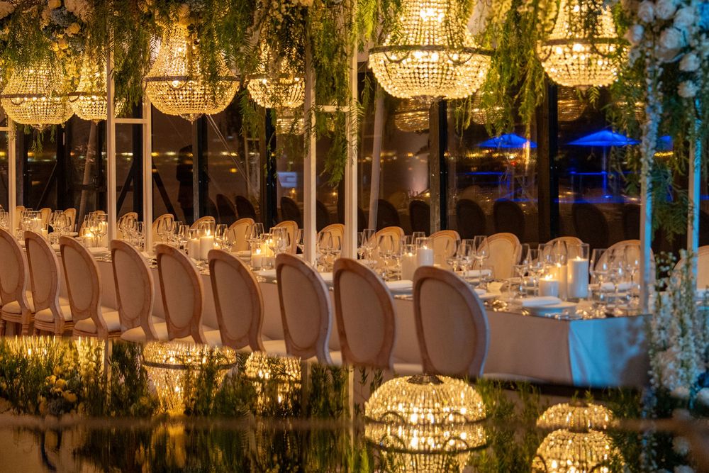Crystal chandeliers illuminate an elegant wedding reception venue with white chairs and romantic evening ambiance.