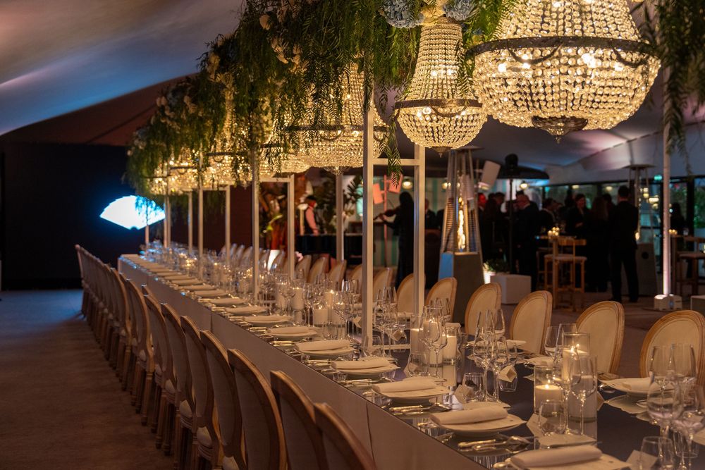 Crystal chandeliers hang above elegant table settings in a luxurious banquet hall with warm lighting and modern decor.
