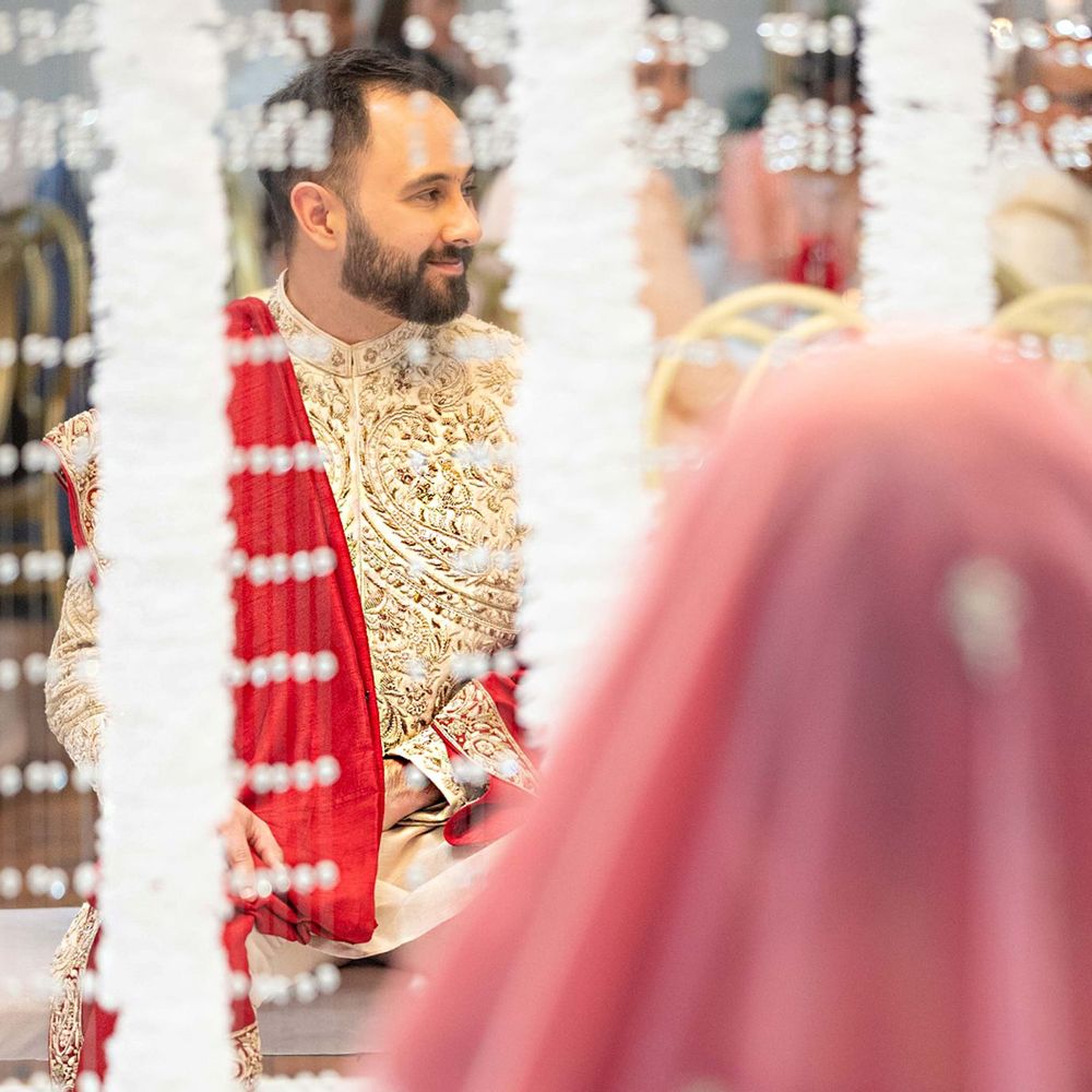 South Asian groom in gold sherwani at traditional wedding ceremony with floral decor.