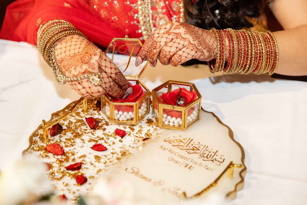 Indian bride with henna hands performs nikah ceremony with ring boxes on decorated wedding tray.