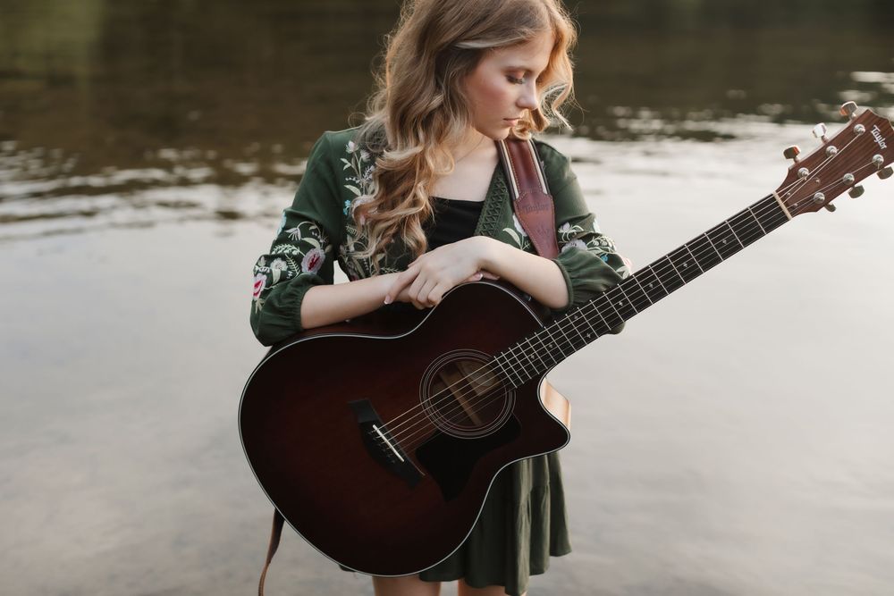 Rachel Delong, Christian musician, wears an embroidered green dress holding her guitar while standing in a lake for a portrait in a lake.