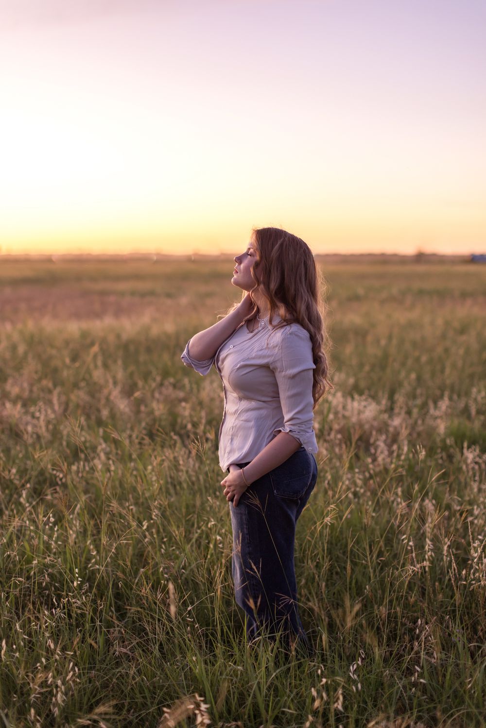 Rachel Delong, Christian musician, wears a pink shirt and jeans poses gracefully in a wheat field at sunset for a portrait in Waco, Texas.