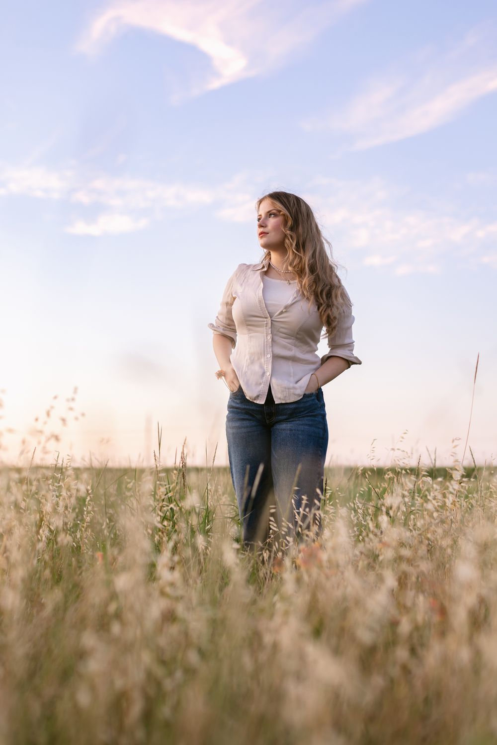 Rachel Delong, Christian musician, wears a pink shirt and blue jeans standing in a field at sunset for a portrait in Waco, Texas.