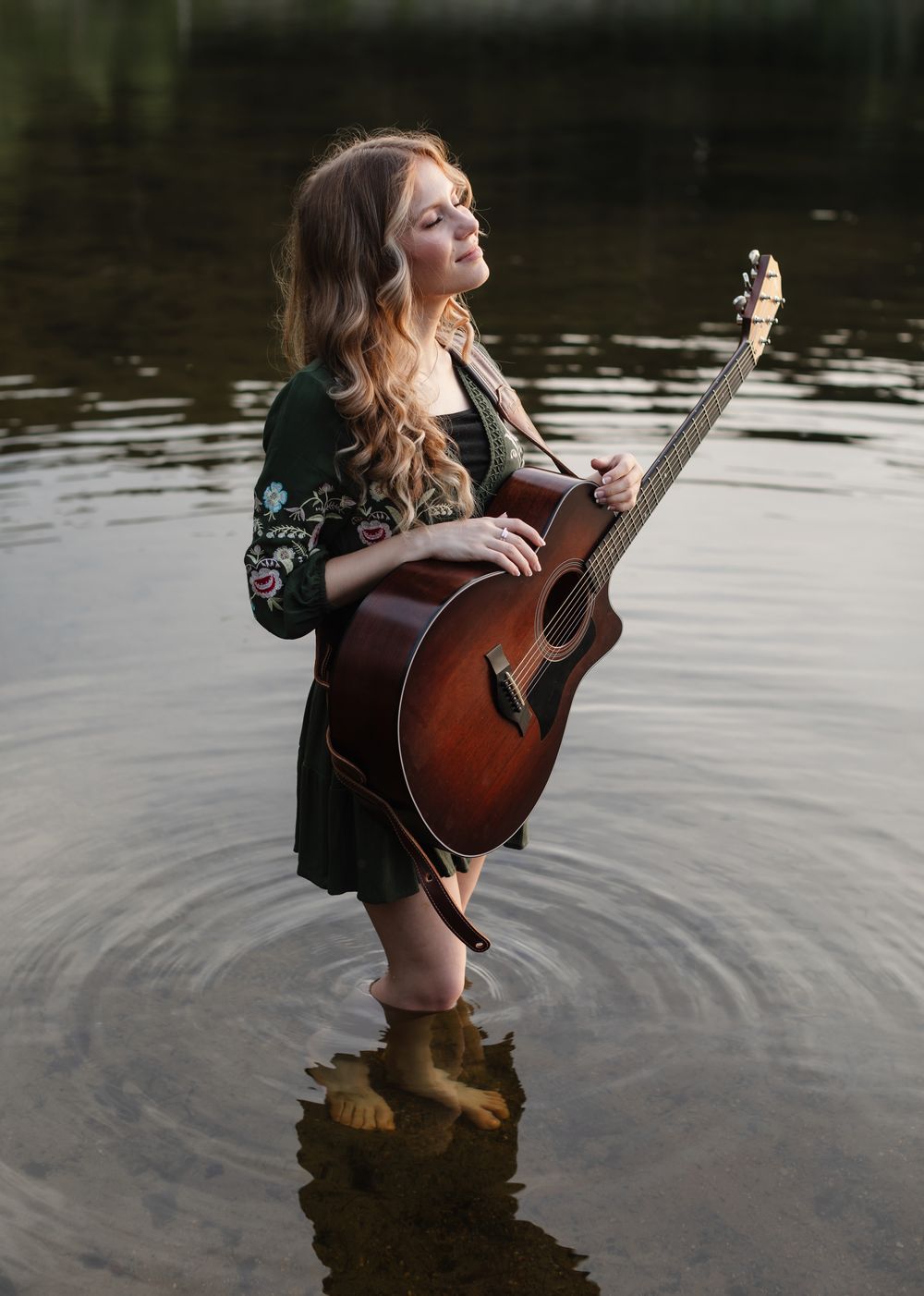 Rachel Delong, Christian musician, stands in Lake Sunapee New Hampshire wearing a green dress and holding her guitar for a peaceful portrait