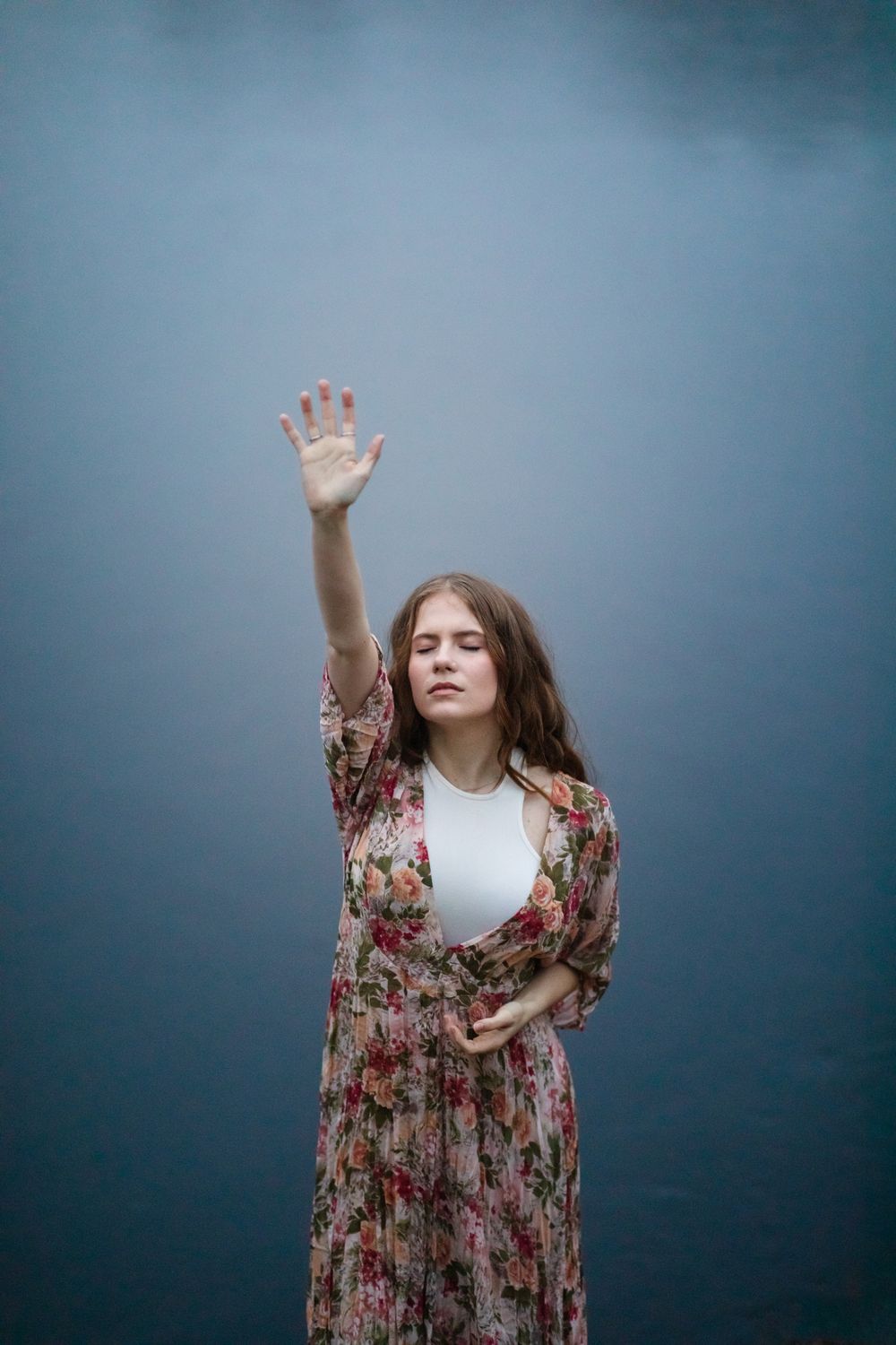 Rachel Delong, Christian musician, raises her hand in worship next to a river for portraits in Concord, Massachusetts.