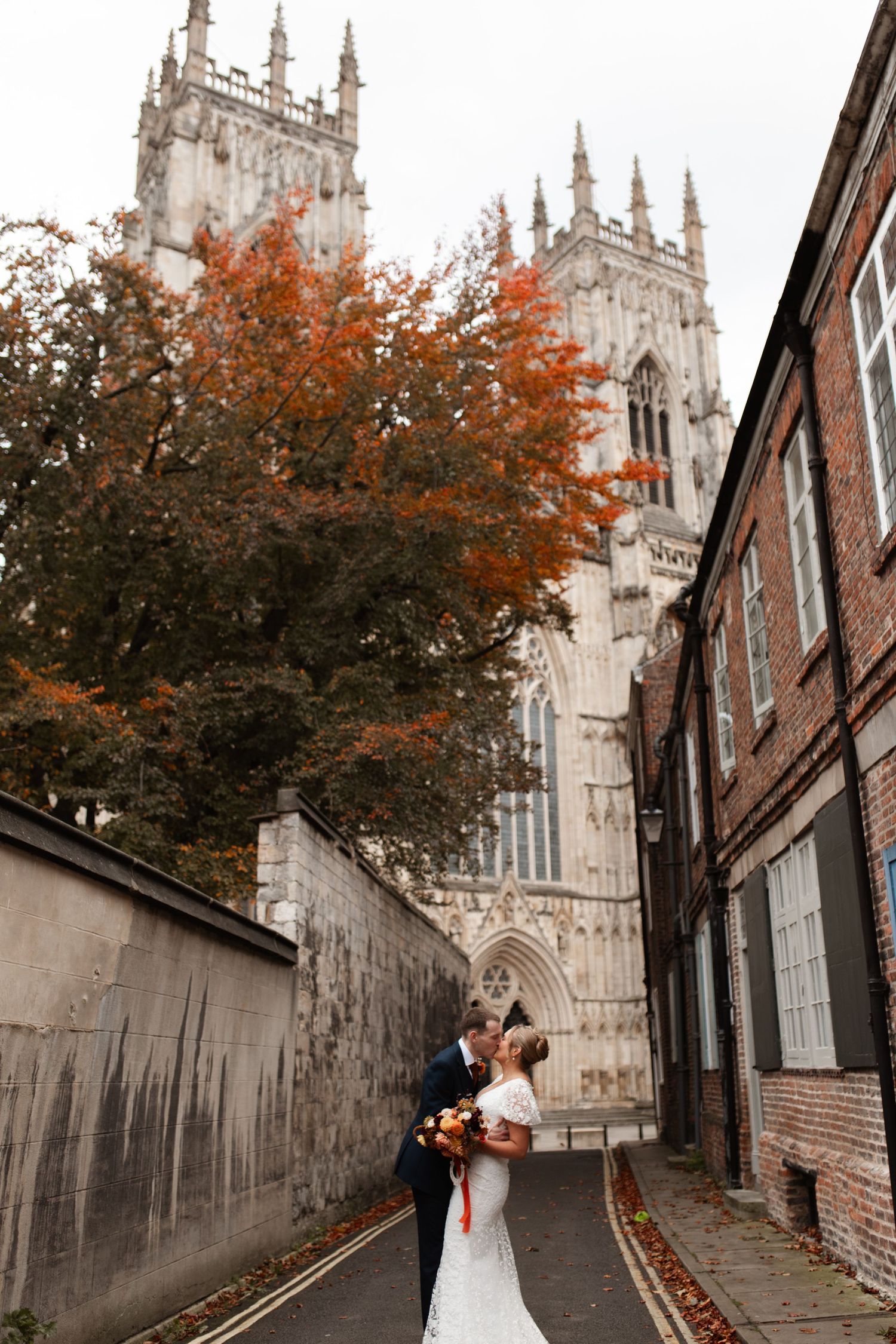 Gothic spires of York Minster cathedral rise above a romantic autumn scene along a narrow cobblestone street.