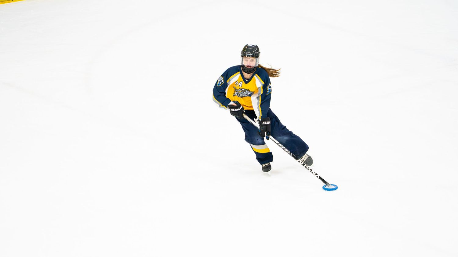 Ringette player in yellow and black uniforms skating during a game.