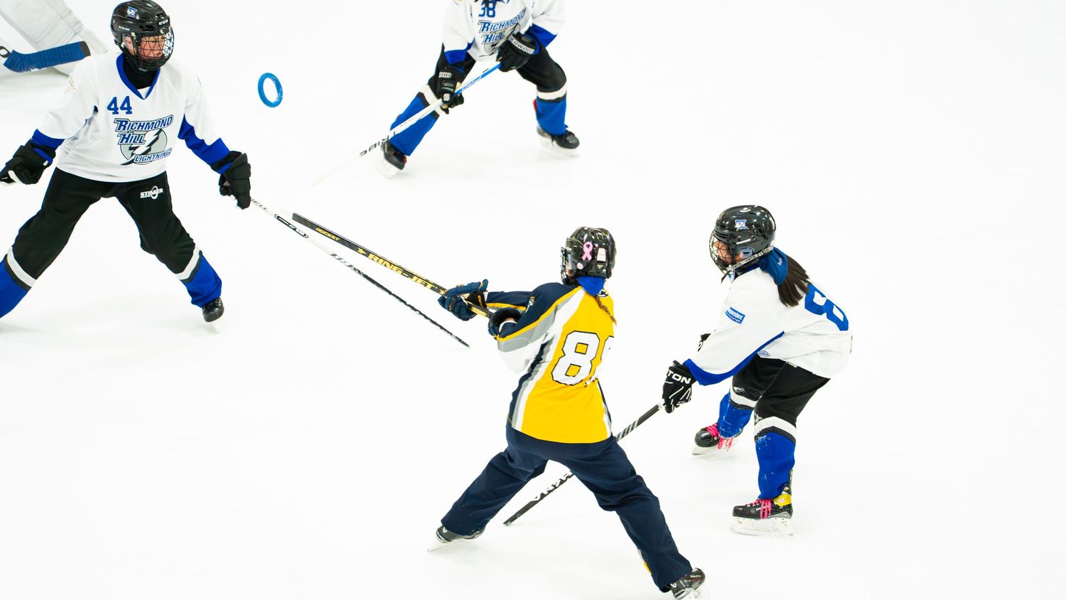 Ringette player in blue and yellow uniforms competing during a Ringette match.