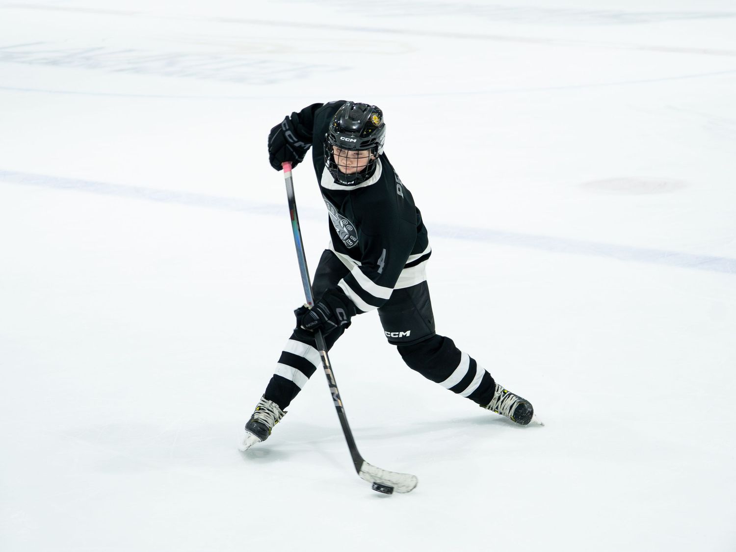 Hockey player in black uniform takes shot on ice during game.