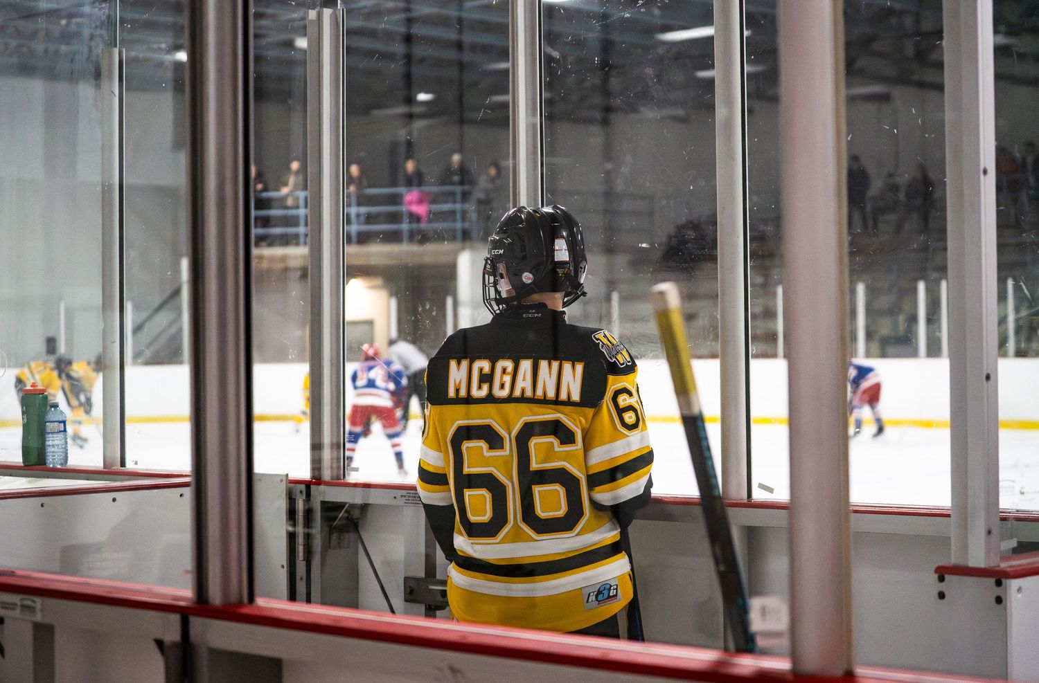 Hockey jersey with number 66 and name McCann viewed through glass at ice rink.