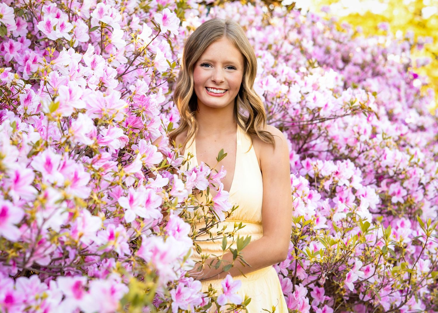 Someone in a yellow dress poses among vibrant pink cherry blossoms on a bright spring day.