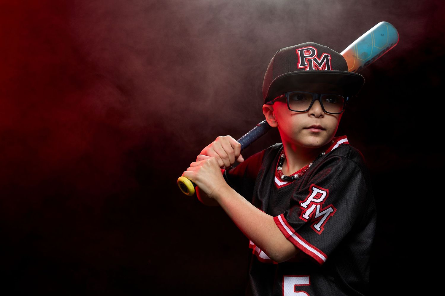 Baseball player in dark uniform with red accents holds bat in ready stance at home plate during night game.