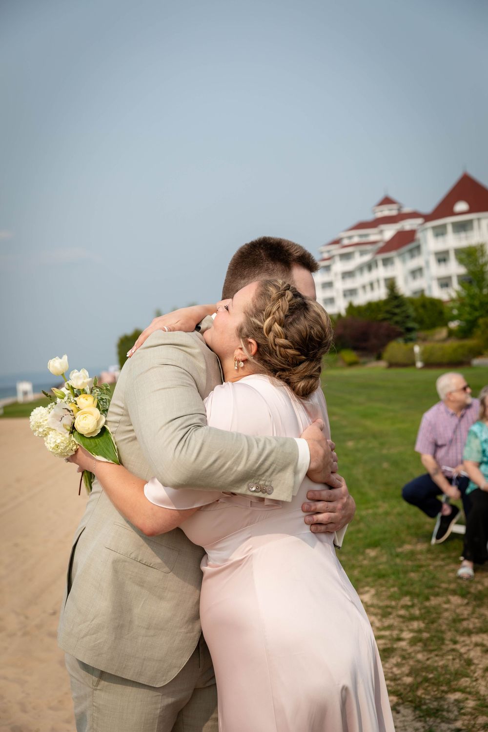A romantic beach wedding moment with a couple embracing against a coastal backdrop with white buildings on a hill.