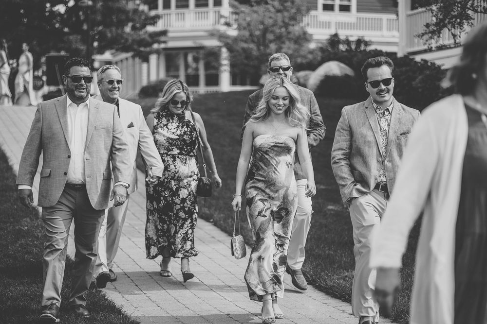 Black and white photo of wedding guests walking along a garden path at an outdoor celebration.