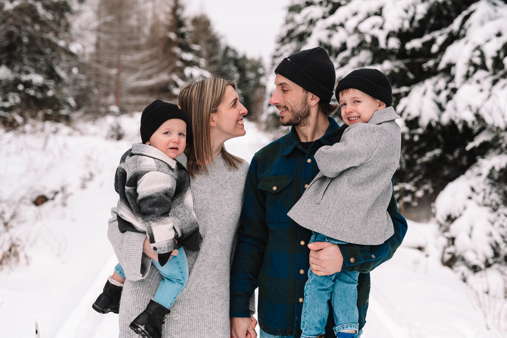 A family shares joyful moments together in a snowy winter landscape with evergreen trees in the background.