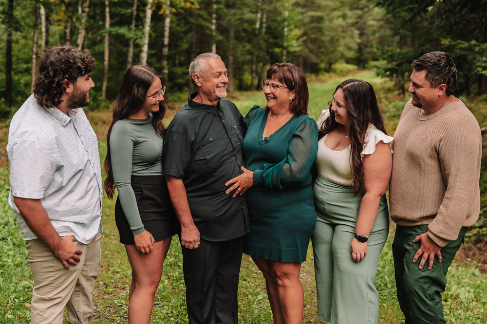 A group of people wearing coordinated green and beige outfits stand together laughing outdoors in nature.
