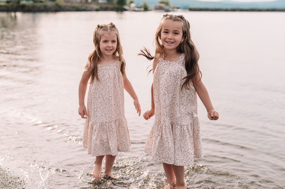 Two children in matching lace dresses play and splash together at the beach during sunset.