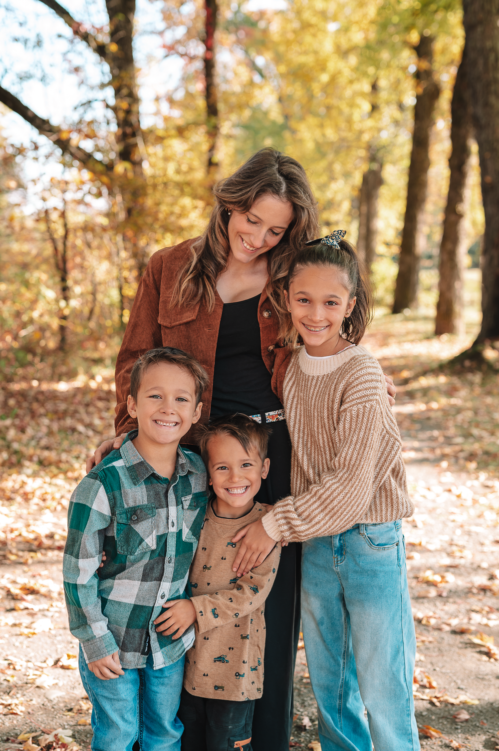 A family embraces outdoors on a sunny autumn day with fallen leaves scattered on the ground.