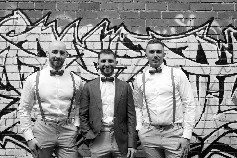 Wedding party poses against urban brick wall with graffiti art.