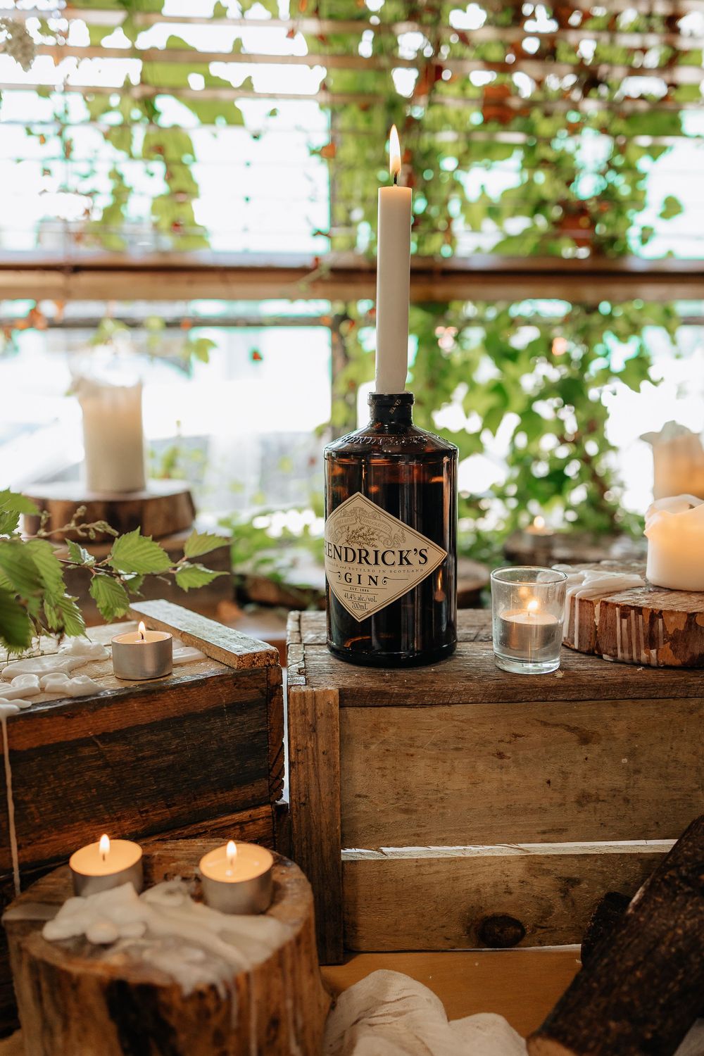 Rustic bar setup with wooden crates, candles, and bottles at wedding reception.