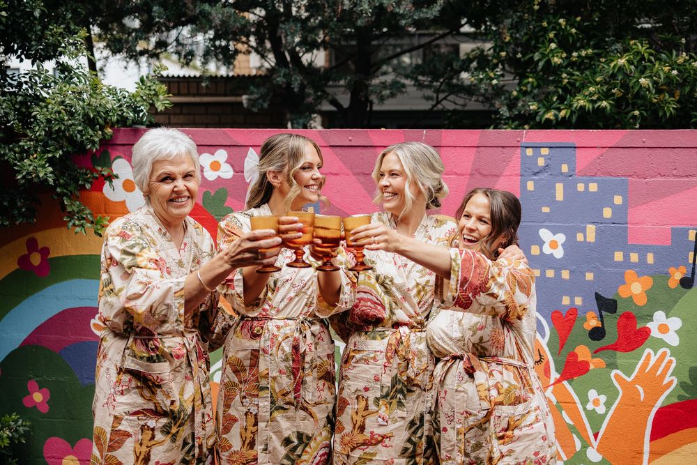 Group wearing matching floral robes posing outdoors in front of colorful wall art.