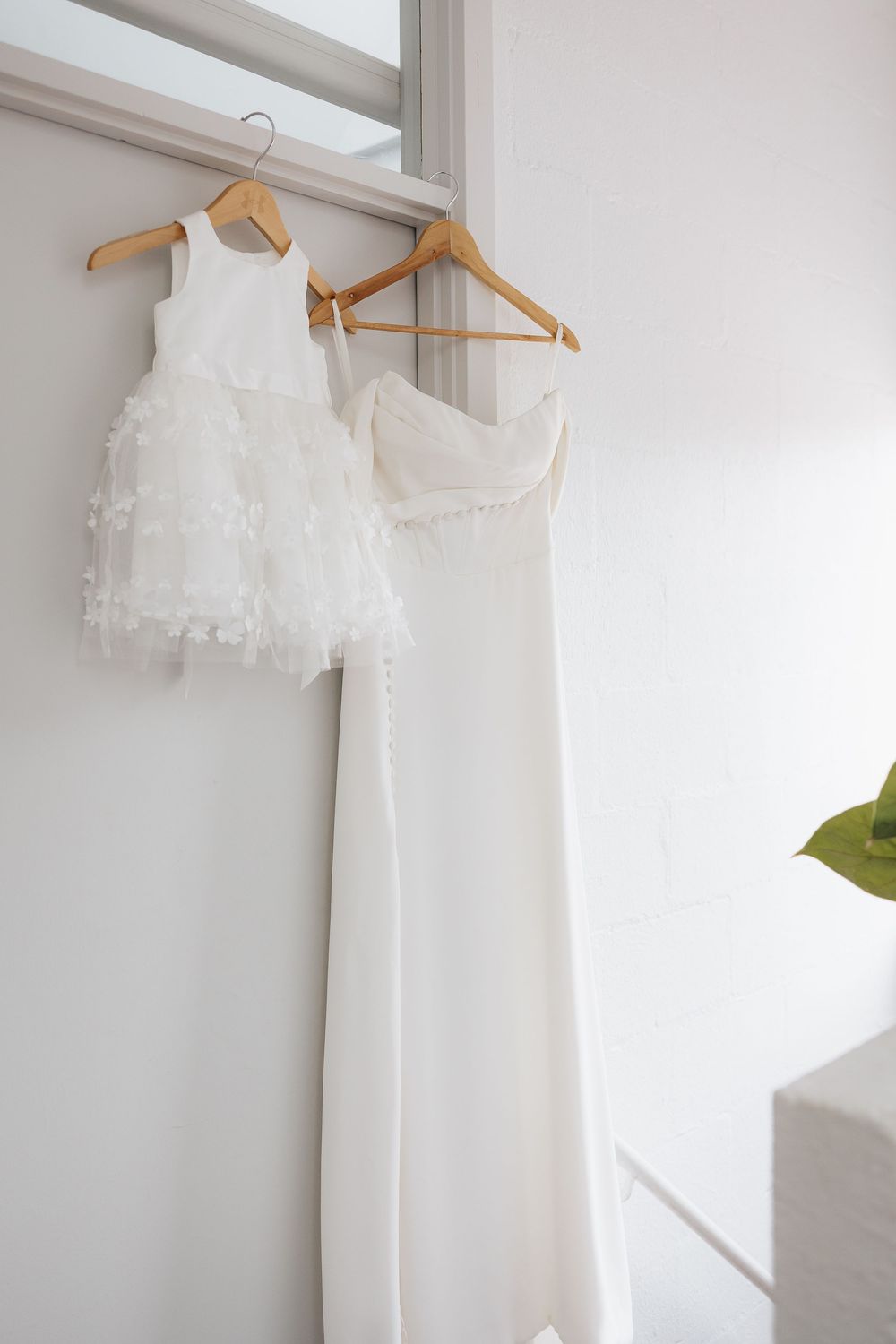 White wedding dresses hanging on wooden hangers against a light colored wall.