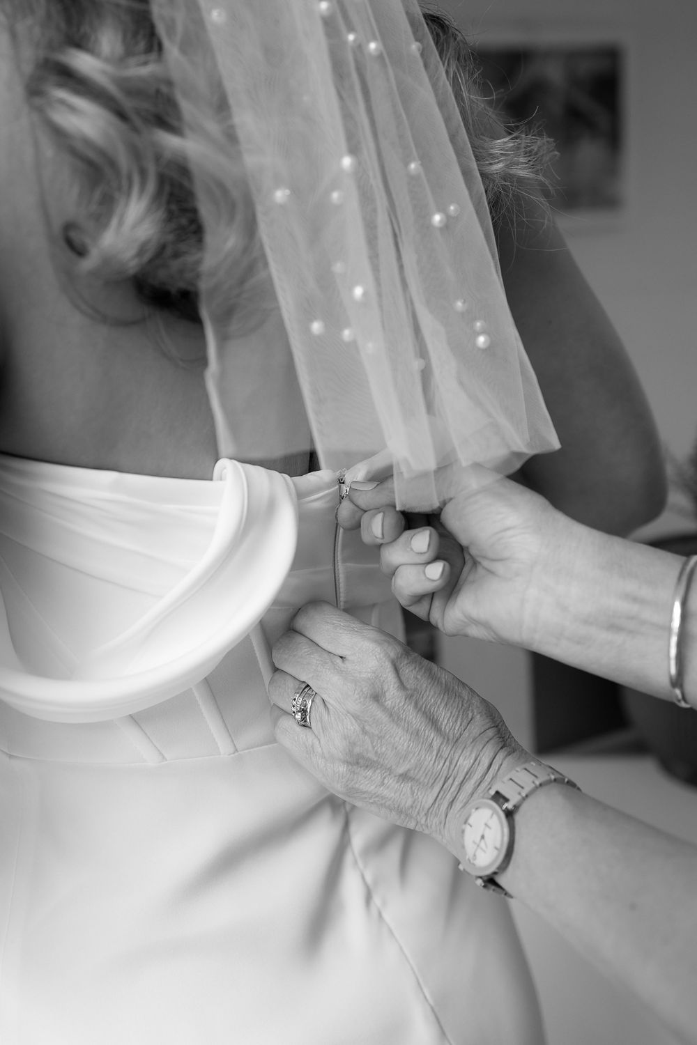 Close-up details of a wedding dress being buttoned up, showing delicate white fabric and lace.