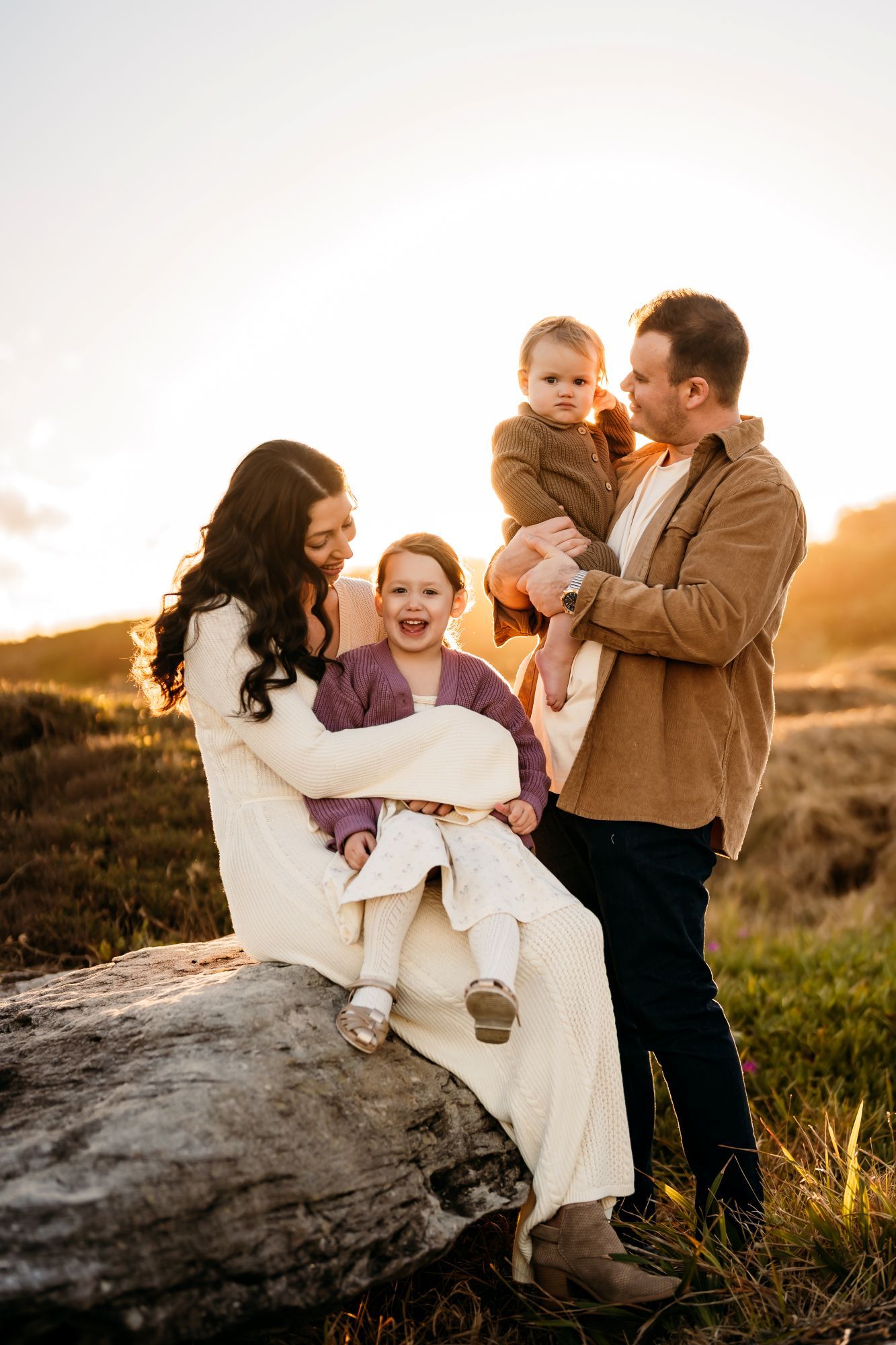 A family shares joyful moments together during golden hour sunset on a rocky hillside outdoors.