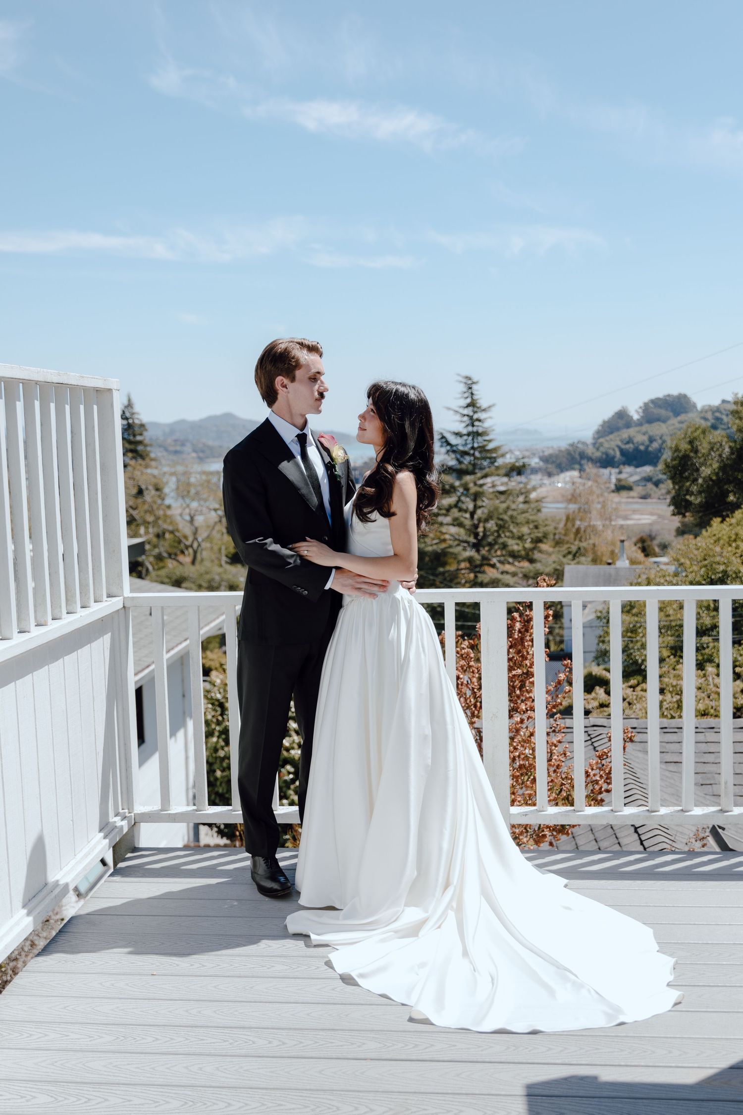 Couple in wedding attire shares romantic moments on a white porch overlooking scenic mountain views on their special day.