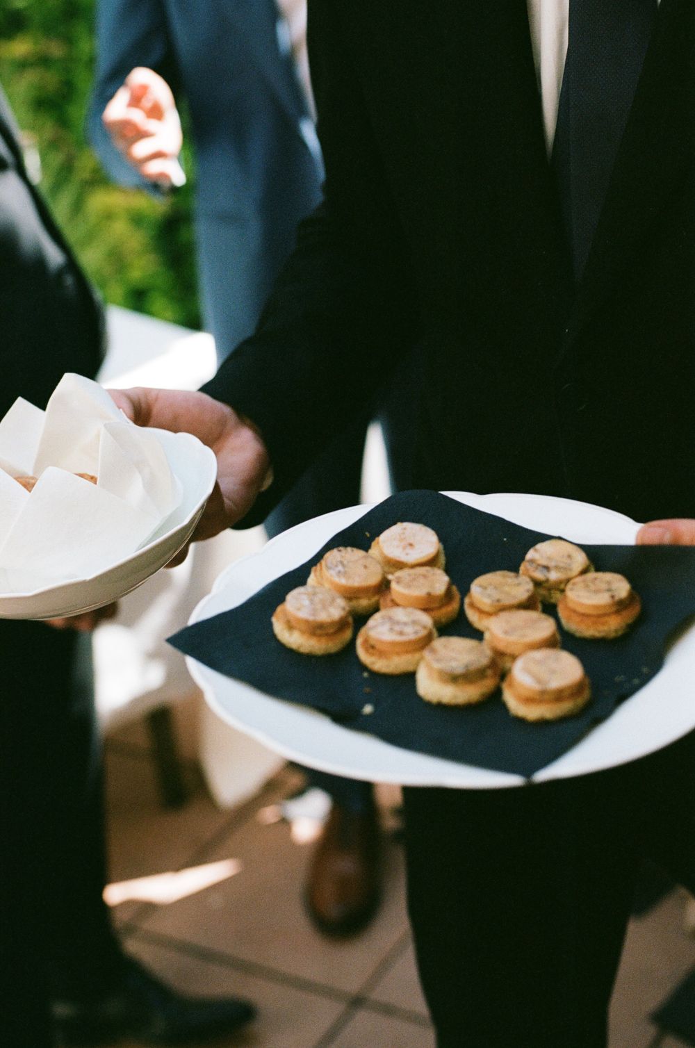 Server carrying small appetizers on white plates at an elegant event.