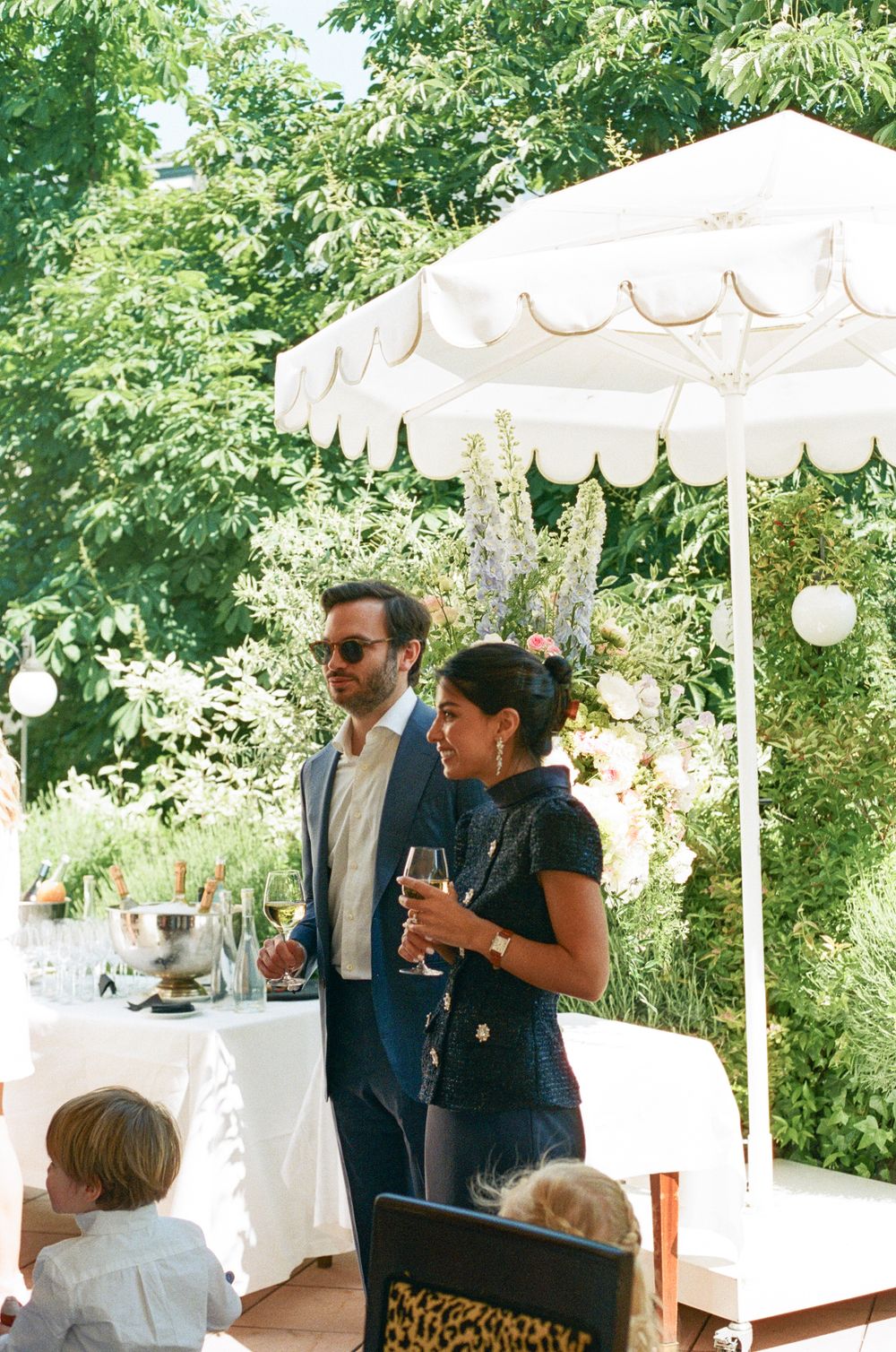 Guests gather under elegant white outdoor canopies at a summer garden party with wine glasses and refreshments. Paris wedding film photo.