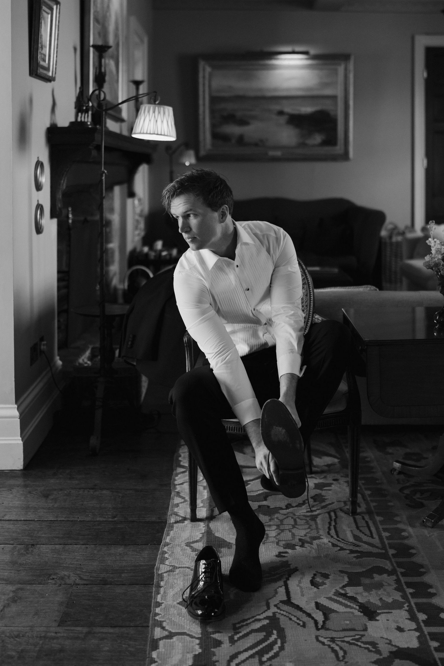 groom getting ready, sat in chair putting his shoes on at dewsall court in herefordshire