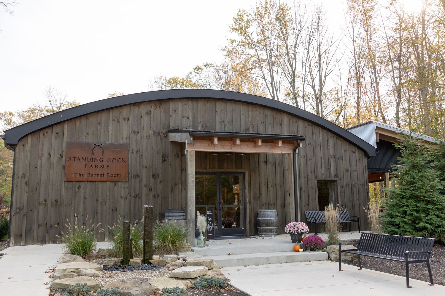 A series of rustic wooden buildings with curved roofs form a nature center or educational facility in a wooded setting.