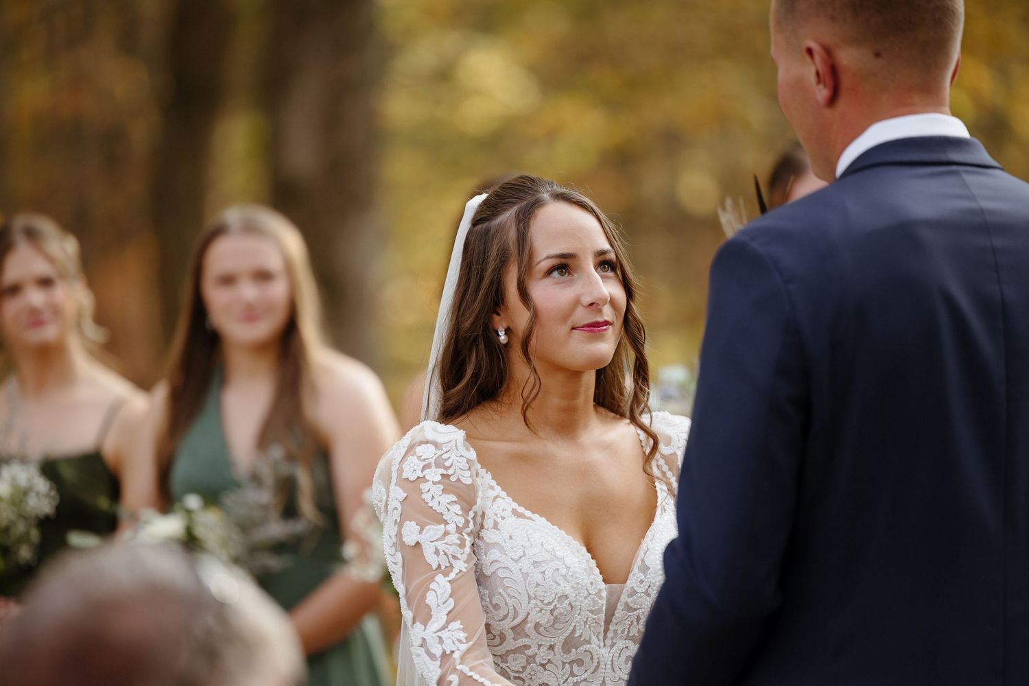 A couple exchanges vows during an autumn outdoor wedding ceremony with bridesmaids watching in the background.
