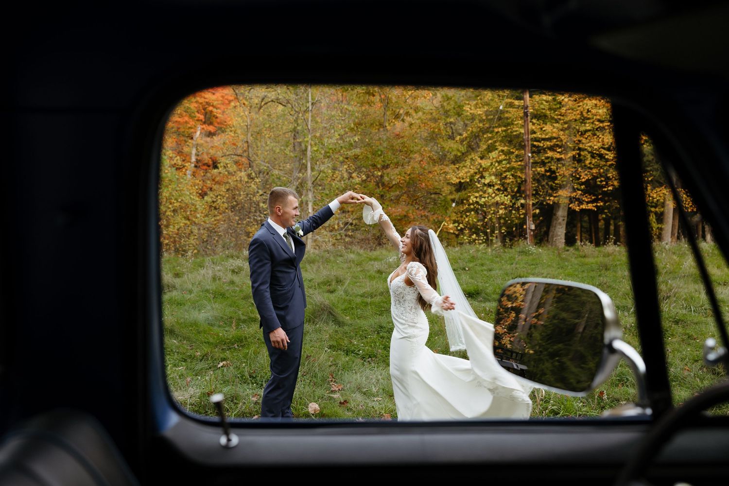 Couple in wedding attire poses for romantic fall photos in a wooded park setting with autumn foliage.
