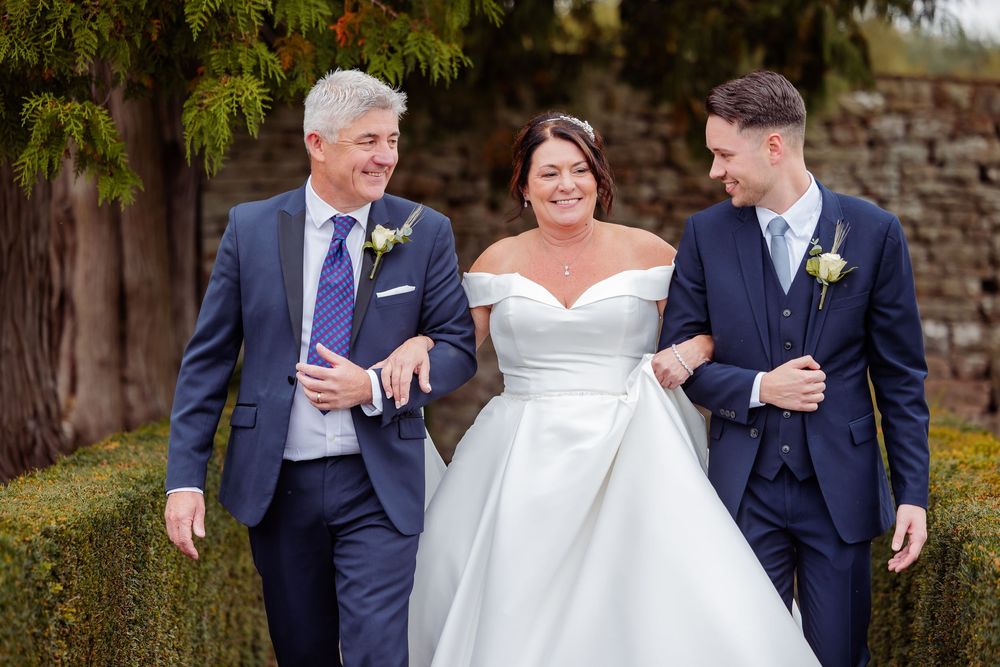 A wedding party in navy suits and white dress share joyful laughter together outdoors.