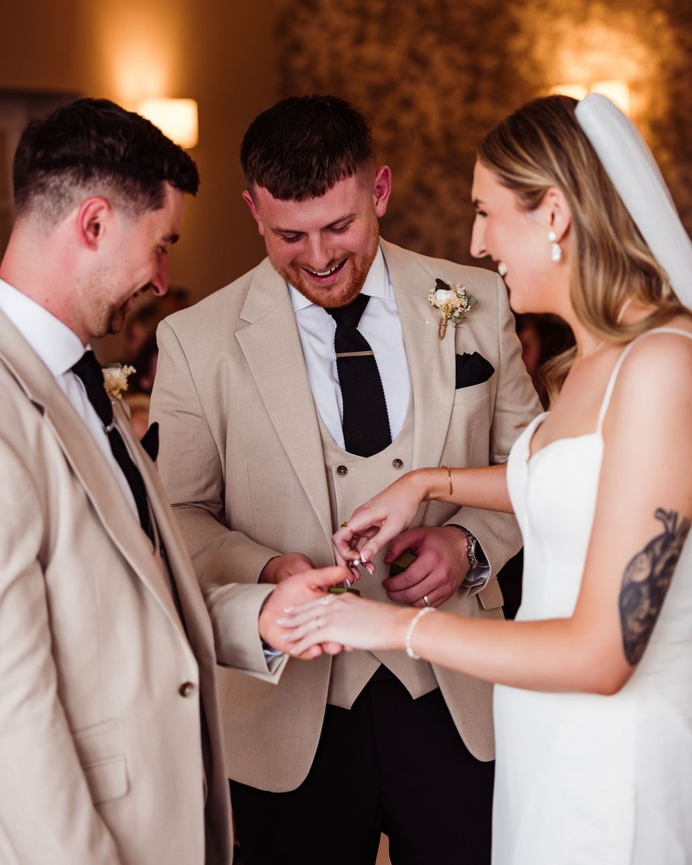 Wedding party members in light colored suits gather in a candlelit room during a formal celebration.